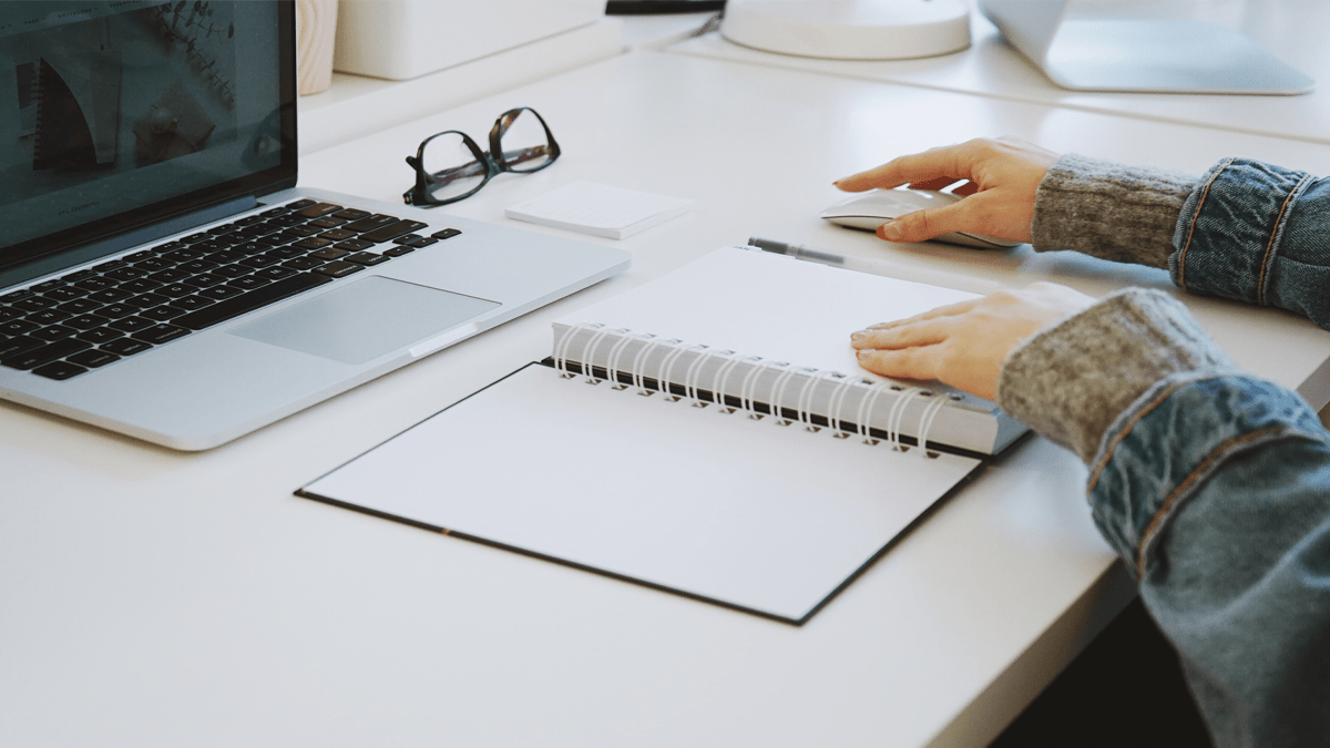 Image of hands with a notebook, pencil, and computer.