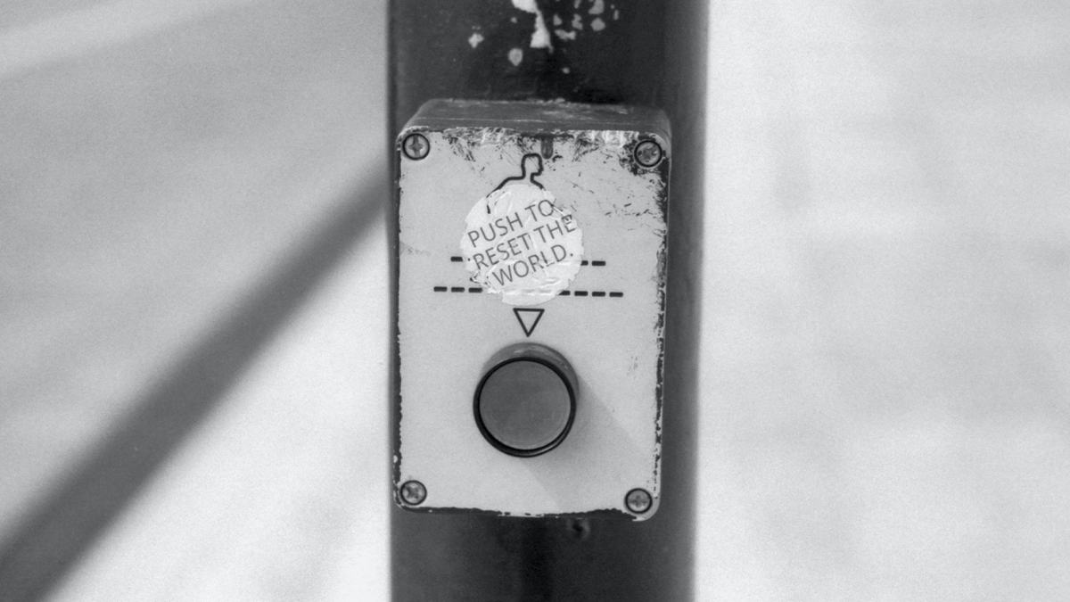 Pedestrian crossing button with sticker that says "PUSH TO RESET THE WORLD"